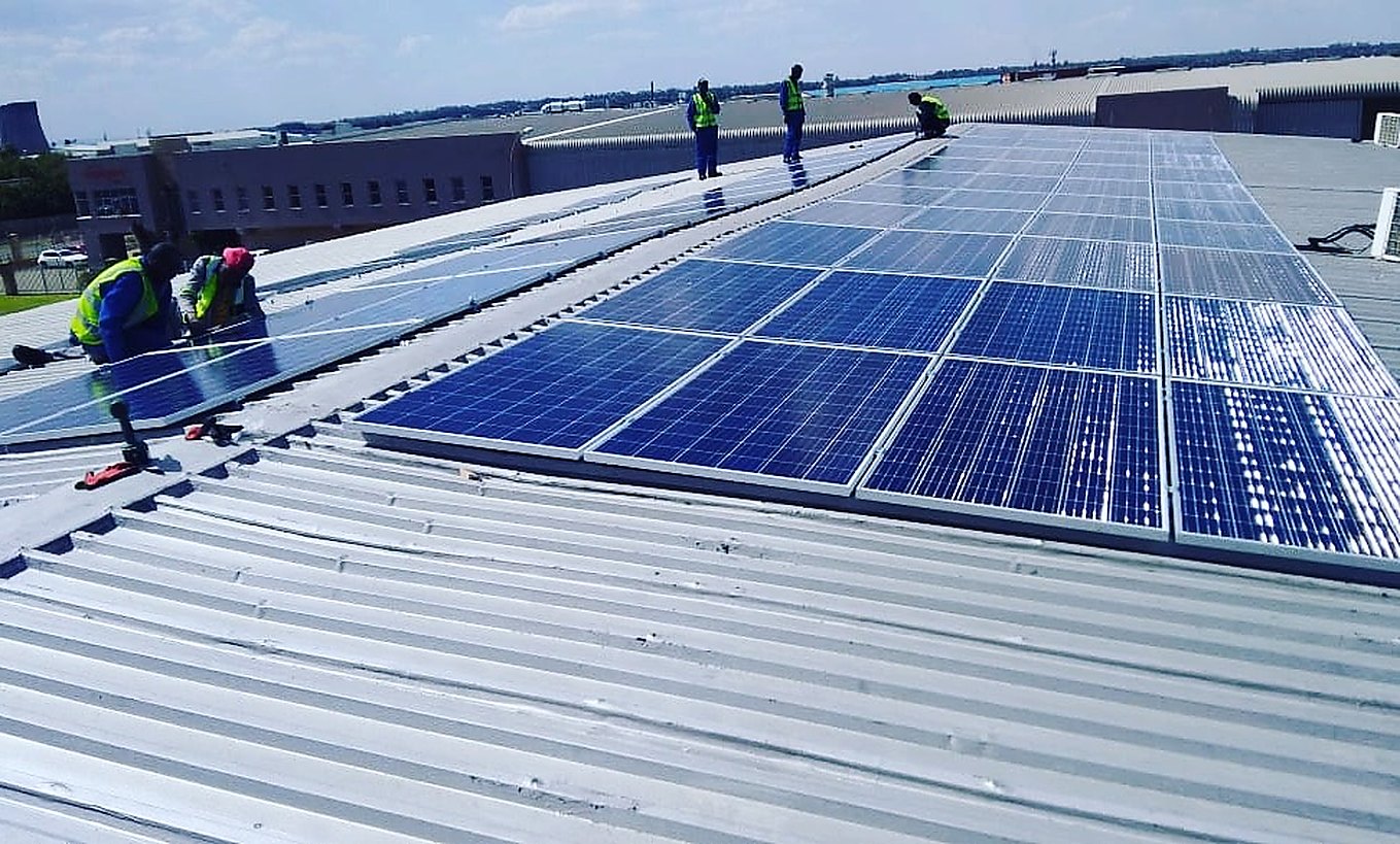 The Affordable Solar Electricity crew laying a panel array across the corrugated roof of an industrial building.